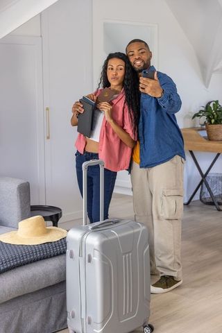 Couple taking selfie before departure holding passport and suitcase in modern loft