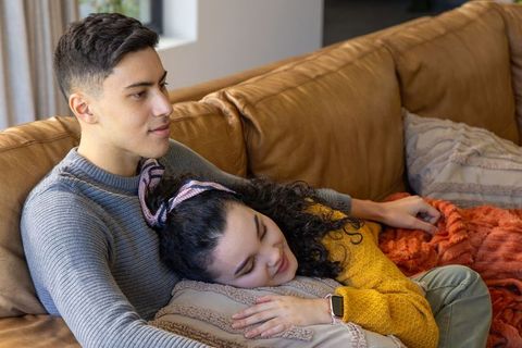 Young couple cuddling on leather sofa during cozy afternoon at home, relaxing together