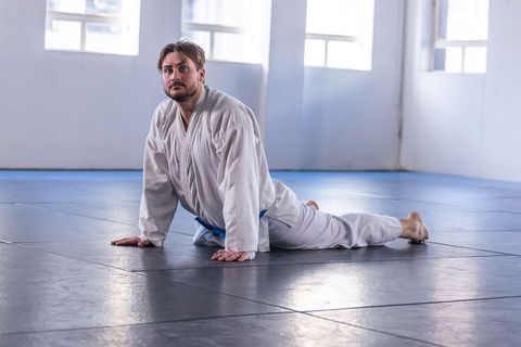 Martial artist stretching in dojo with white gi and blue belt