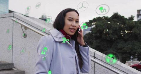 Asian woman speaking on smartphone amid augmented reality eco icons on urban stairway