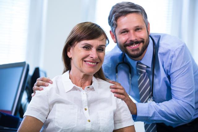 Male doctor with stethoscope smiling and standing next to a happy female patient in a hospital setting. Ideal for use in healthcare advertisements, medical websites, patient care brochures, and wellness blogs to depict trust and positive doctor-patient relationships.