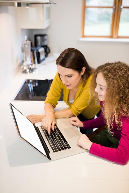 Mother and daughter using laptop in kitchen at home
