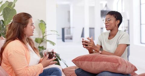Two women sharing coffee and conversation in bright modern office breakroom, collaboration