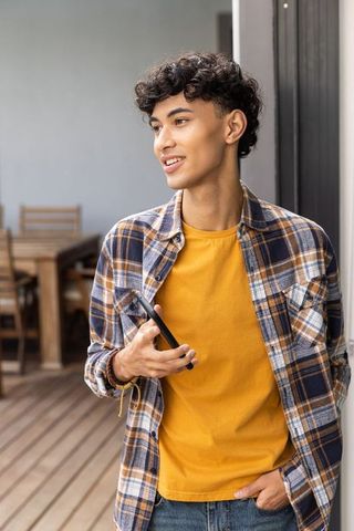 Young Man in Yellow T-shirt Holding Smartphone on Wooden Deck