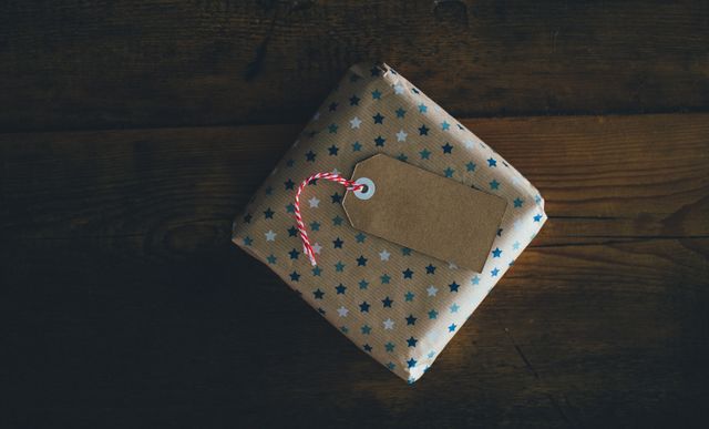 Gift wrapped in star patterned paper with a blank tag, resting on a wooden surface. Ideal for birthday, holiday, or celebration themes, and conveying a sense of surprise and joy in digital and print projects.