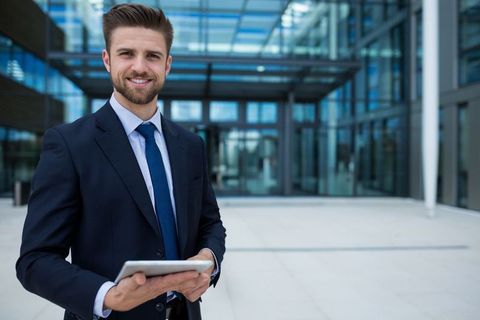 Confident professional with digital tablet outside modern glass building