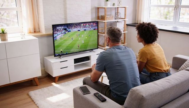 Couple watching soccer on tv, relaxing on sofa with remote in modern living room