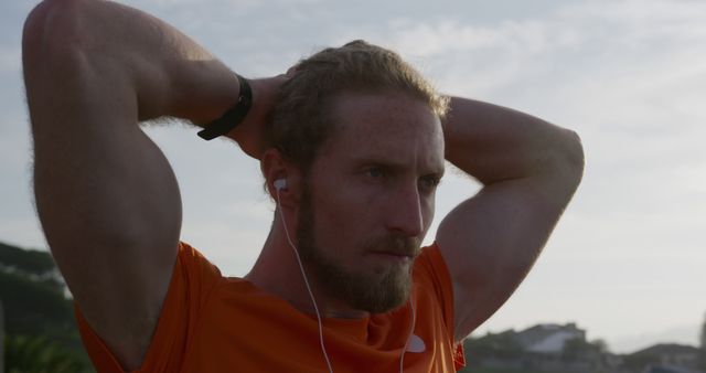 Man preparing for workout, wearing headphones and orange shirt, outdoors. Perfect for fitness and wellness materials, active lifestyle blogs, workout motivation posters, and gym advertisements.