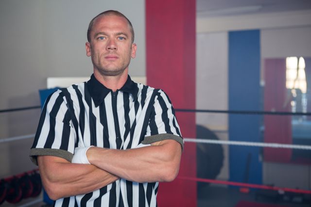 Referee standing confidently with arms crossed in a boxing ring. Ideal for use in sports-related content, articles on boxing referees, promotional material for sports events, and training materials for referees.
