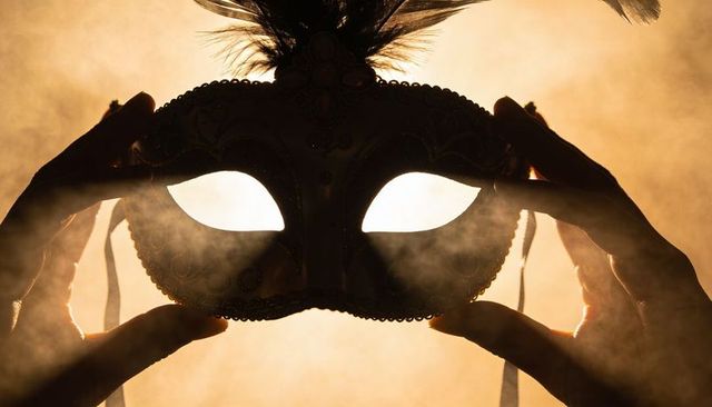 Holding ornate venetian mask with feathers and smoky golden backlight for masquerade ball