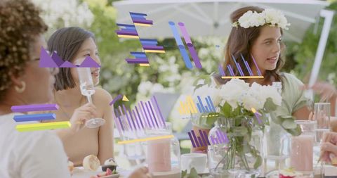 Friends chatting over garden brunch wearing flower crown holding stemware at floral table