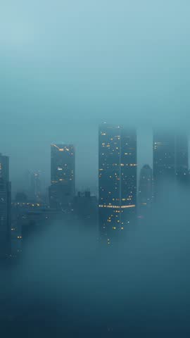 Vertical city skyline video with skyscrapers drifting through dense fog and glowing windows