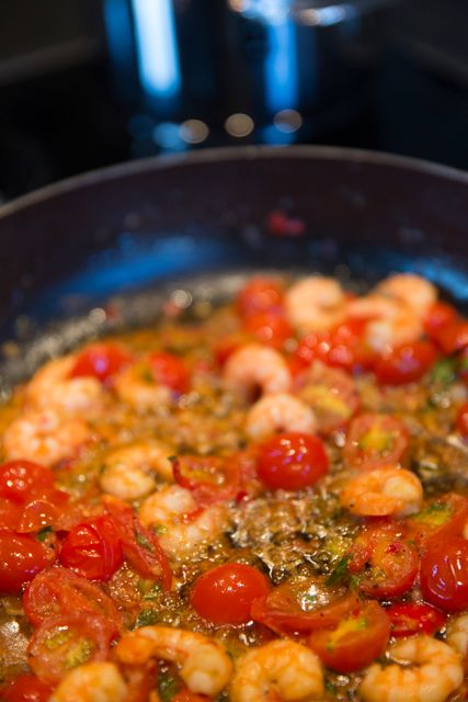 Fresh shrimp and cherry tomatoes sautéing in skillet with bubbling sauce. Ideal for illustrations on cooking techniques, seafood recipes, culinary arts, and food presentation. Suitable for use in blogs, cookbooks, cooking websites, and restaurant menus.