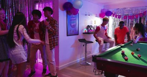 Diverse friends celebrating birthday, playing pool and chatting in neon-lit game room