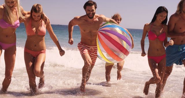 Group of friends running and playing with a colorful beach ball on a sandy beach. Perfect for themes of summer vacation, friendship, joy, outdoor activities, carefree moments, and travel promotions. Ideal for advertisements, banners, websites, and magazines focusing on beach activities and energetic lifestyles.