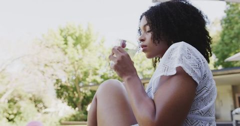 African american woman relaxing on backyard patio sipping drink in white lace top outdoor