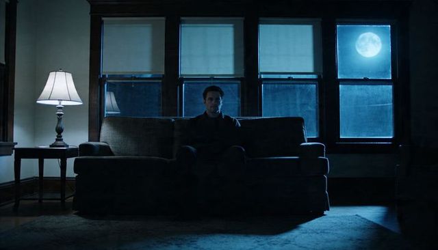 Solitary man sitting on sofa under moonlight in dim living room, moody night solitude