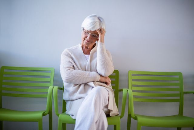 Tensed senior woman sitting on chair in waiting area of hospital