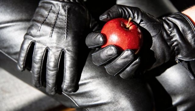 Black leather gloves holding red apple closeup dramatic moody texture and stitching