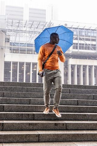 African american man walking down steps holding blue umbrella in rain urban commuter lifestyle