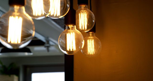 Illuminated Edison bulbs hang against a warm background, creating a cozy and inviting atmosphere. Their vintage design adds a touch of nostalgia and charm to the modern interior.