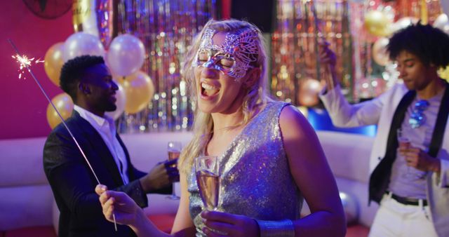 Image of happy caucasian woman in mask dancing with sparkler and glass of champagne at a nightclub. Fun, drinking, going out and party concept.