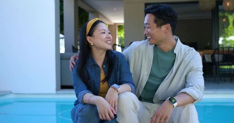 Couple sharing embrace on pool edge at modern patio while wearing denim and smartwatches
