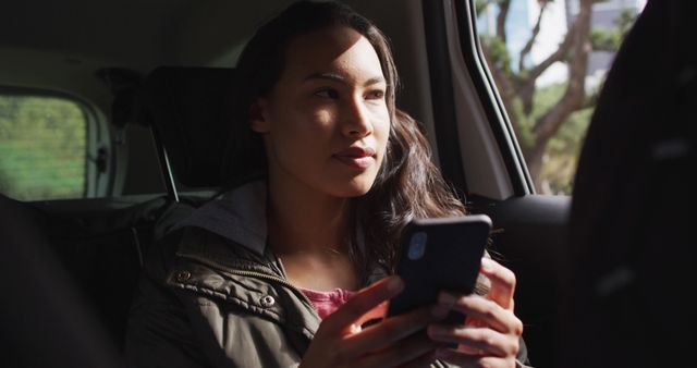 Asian woman smiling while looking out of the window and using smartphone in the car. modern lifestyle and living concept