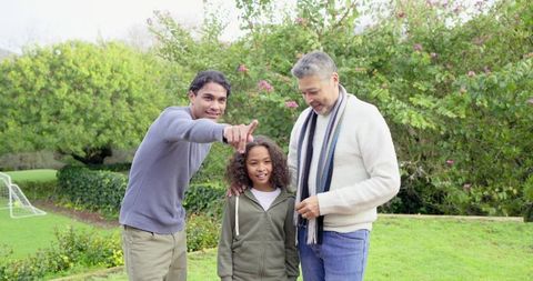 Multiracial fathers pointing with smiling child on garden lawn near youth soccer goal