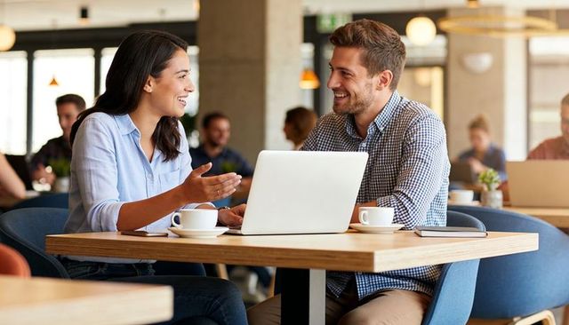 Smiling coworkers collaborating over laptop in modern cafe workspace with coffee