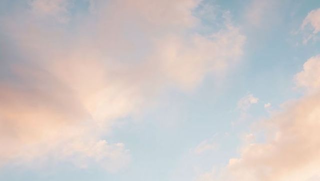Dreamy pastel sunrise sky with peach-pink clouds and soft blue gradient