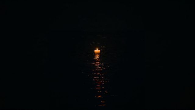 Floating candle casting warm flame reflection on dark water at night minimalist solitude