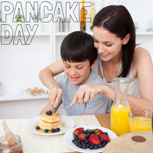 Perfect for illustrating family bonding moments around food, this image captures a mother and her son joyfully celebrating Pancake Day. The family-friendly breakfast setting, featuring delicious pancakes topped with berries and a glass of orange juice, creates a warm and inviting scene. Ideal for use in articles, advertisements, and promotions related to family meals, healthy eating, and culinary celebrations.