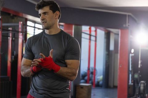 Boxer wrapping hands preparing for intense gym workout, focused male athlete training