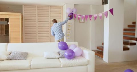 African American man decorating living room with purple balloons and bunting for party