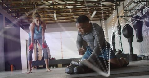Female trainee watching male coach holding focus mitts during boxing training session
