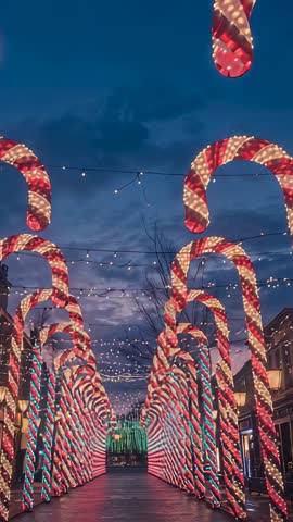Tilting vertical video revealing dusk over festive candy-cane archway with twinkling lights
