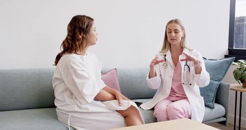 Female doctor consulting patient on sofa in bright clinic, explaining treatment plan