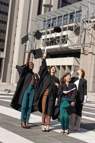 Diverse female graduates celebrating urban campus throwing mortarboards and holding diplomas