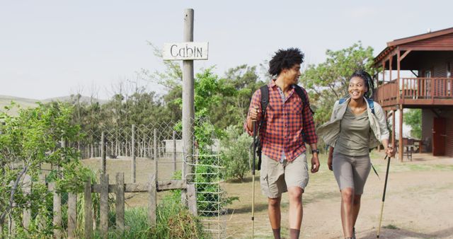 Happy african american couple with backpacks, hiking with trekking poles together, slow motion. Lifestyle, domestic life, countryside and nature concept.