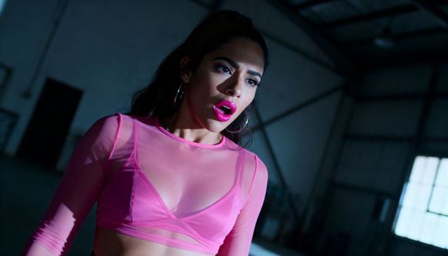 Singing hispanic woman in sheer pink crop top and bralette in cinematic warehouse
