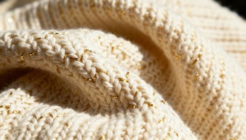 Cream knit close-up featuring gold metallic thread, ribbed texture and soft wool fibers