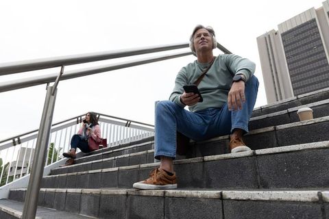 Middle-aged commuter listening to headphones on city overpass stairs holding smartphone