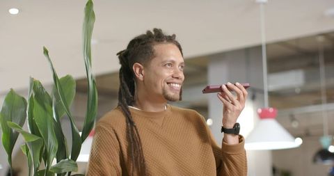 Smiling African American professional speaking into smartphone in bright coworking space