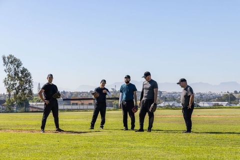Diverse male teammates practicing on baseball infield at suburban park holding gloves