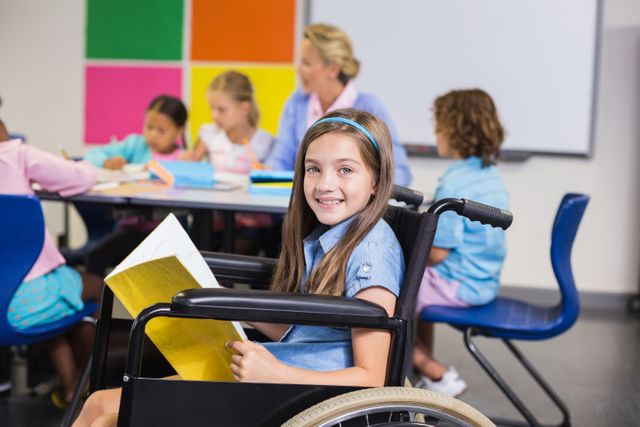 This image depicts a young disabled school girl in a wheelchair, smiling and holding a book in a classroom. Other children and a teacher are visible in the background, engaging in educational activities. This image can be used for educational materials, promoting diversity and inclusion, or illustrating concepts related to disability and special needs in school settings.
