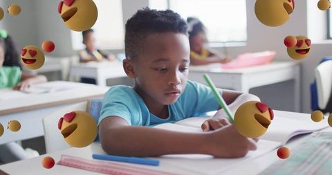 Focused Young Male Student Writing at Desk in Classroom