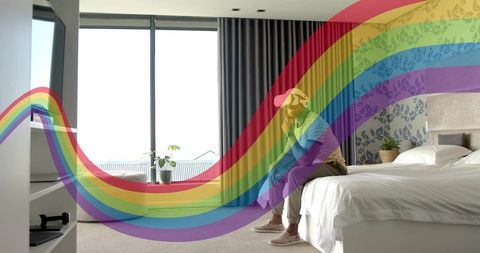 Man wearing cap sitting on bed holding phone in modern minimalist bedroom with rainbow overlay