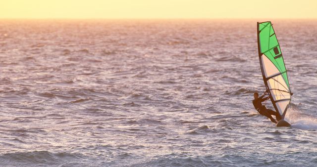 Windsurfing enthusiast navigating waves on ocean during serene sunset. Suitable for travel blogs, outdoor activity promotions, adventure ads, and summer vacation content.