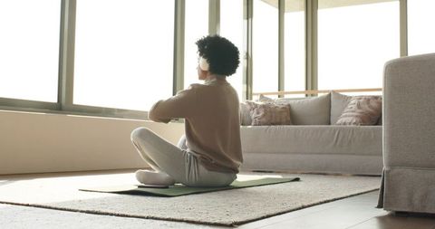 African American man practicing meditation at home with headphones in sunlit living room